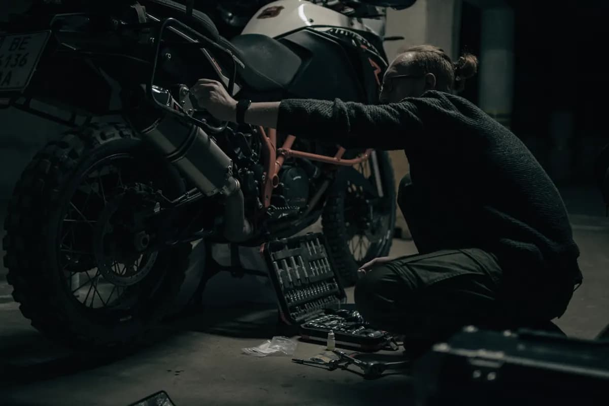 Un mecánico agachado reparando una motocicleta en su taller.